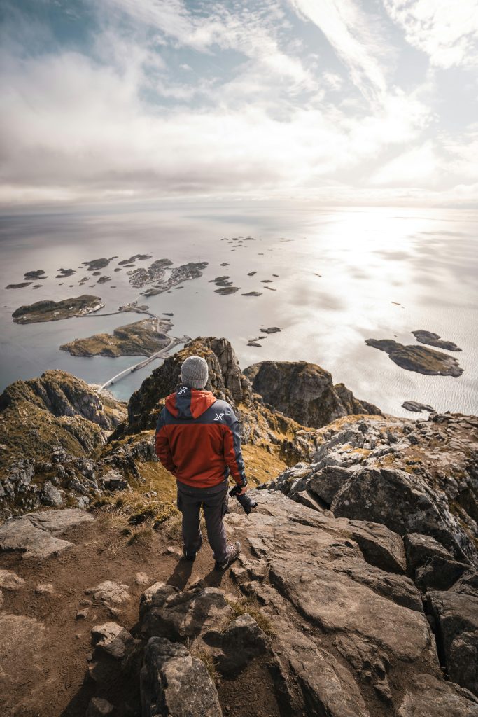 Man explores breathtaking view of Lofoten Islands from mountain peak at sunset.